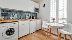 A modern kitchen with a washing machine, microwave, and a dining area with a table and chairs. - 2P Studio With Patio Near Paris (Le Pre-Saint-Gervais)