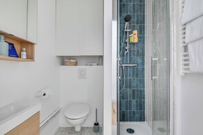 A modern bathroom with a shower, toilet, and a shelf with toiletries. - 2P Studio With Patio Near Paris (Le Pre-Saint-Gervais)