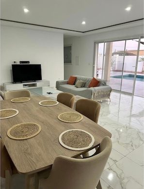 A modern living room with a dining table, chairs, a sofa, and a television. - Villa Jasmin, your corner of paradise for a relaxing stay (Djerba Midun)