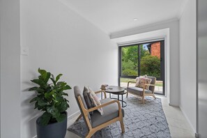 A modern room with a large window, a potted plant, two chairs, a small table, and a rug. - Fully Renovated with Outdoor Fun (CANBERRA)