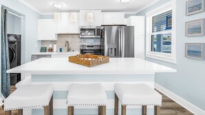 Une cuisine moderne avec des meubles blancs, des appareils en acier inoxydable et un îlot central doté de tabourets de bar.