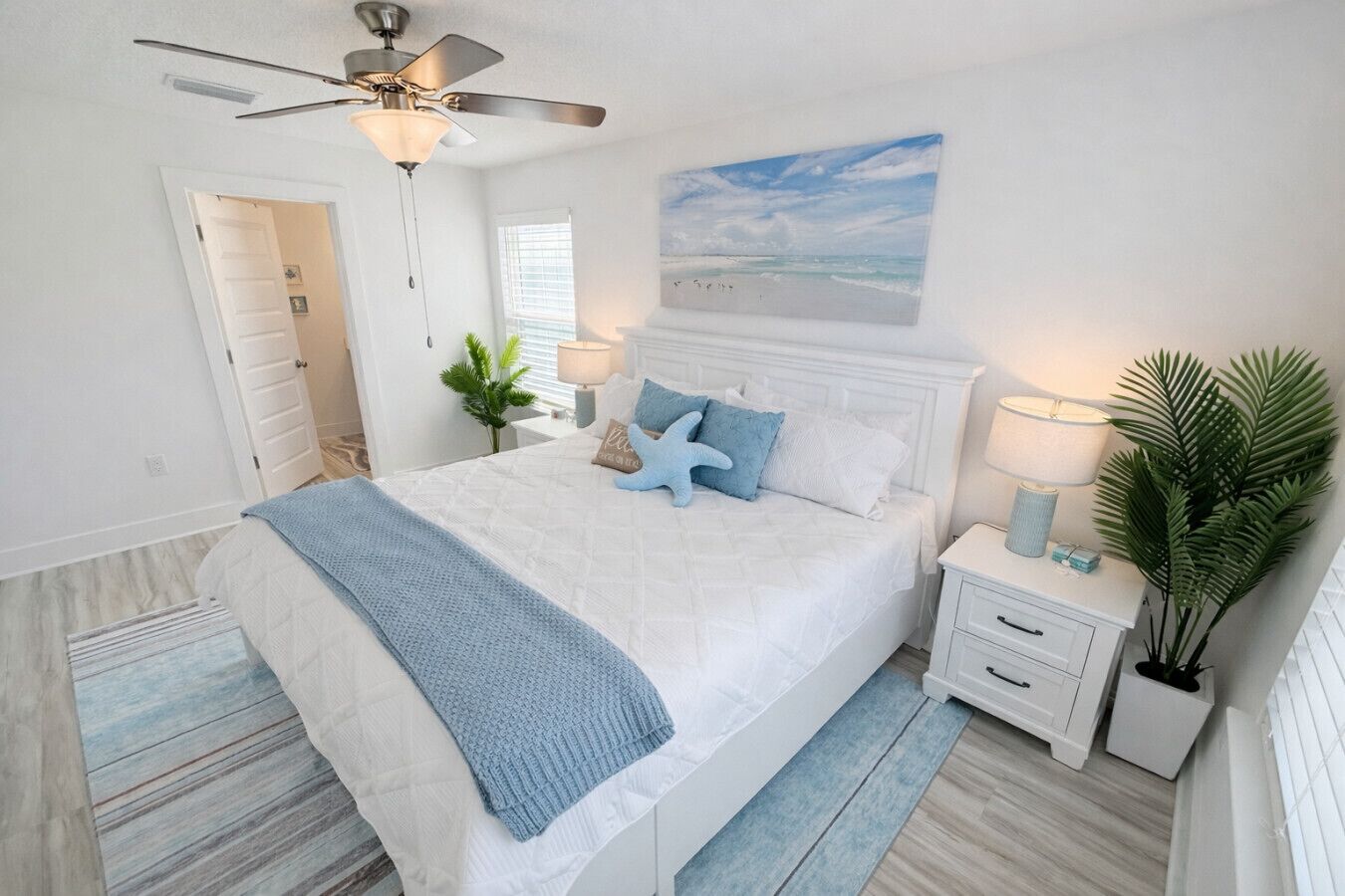 A bedroom with a bed, nightstands, a ceiling fan, a window, and a wall-mounted painting.