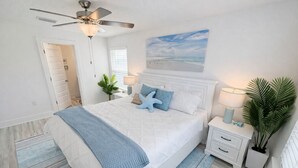 Una camera da letto con un letto, comodini, una ventola a soffitto, una finestra e un quadro appeso al muro.