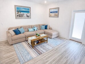 A living room with a beige sectional sofa, a coffee table, and two framed beach paintings on the wall.