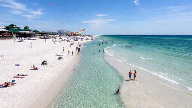 Una spiaggia con acqua cristallina, persone e edifici sullo sfondo.