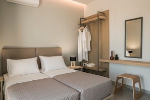 Ein Hotelzimmer mit Bett, Nachttisch, Bademantelständer, Spiegel und einem kleinen Hocker.