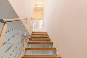 Una escalera moderna con barandillas de vidrio y escalones de madera que conducen a un pasillo luminoso.