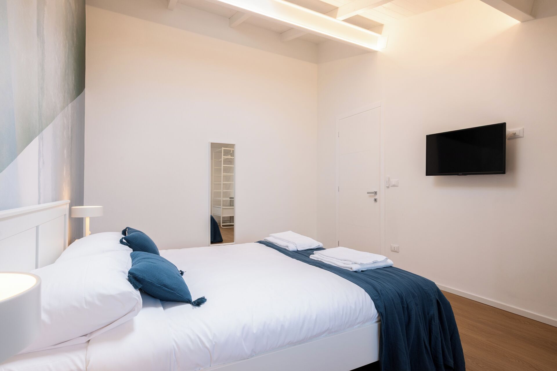 A bedroom with a bed, a TV, a wardrobe, and a mirror.