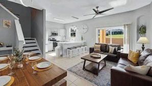 A modern interior with a dining area, a sofa, a coffee table, and a kitchen in the background. - 4Bd 3Ba, (2 Primary), 8.7m to Disney, No Resort Fees! (Davenport)