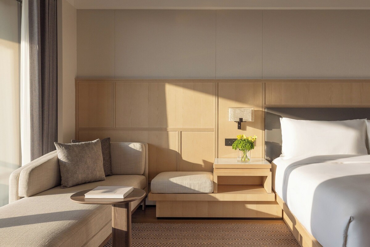 Une chambre d’hôtel comprenant un lit, un canapé, une table de chevet et une lampe fixée au mur.