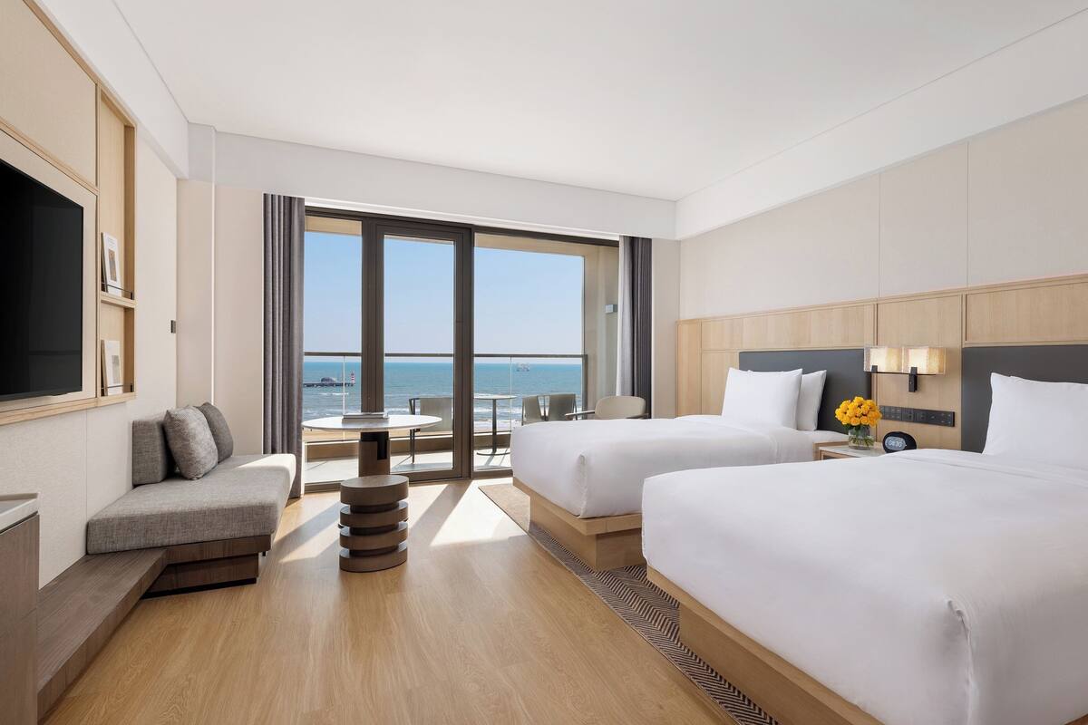 Una habitación de hotel con dos camas, un sofá, una mesa y vista al mar.