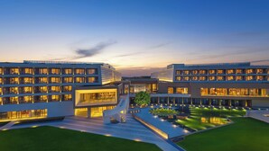 A modern multi-story hotel with a central courtyard, outdoor seating, and a well-lit facade.