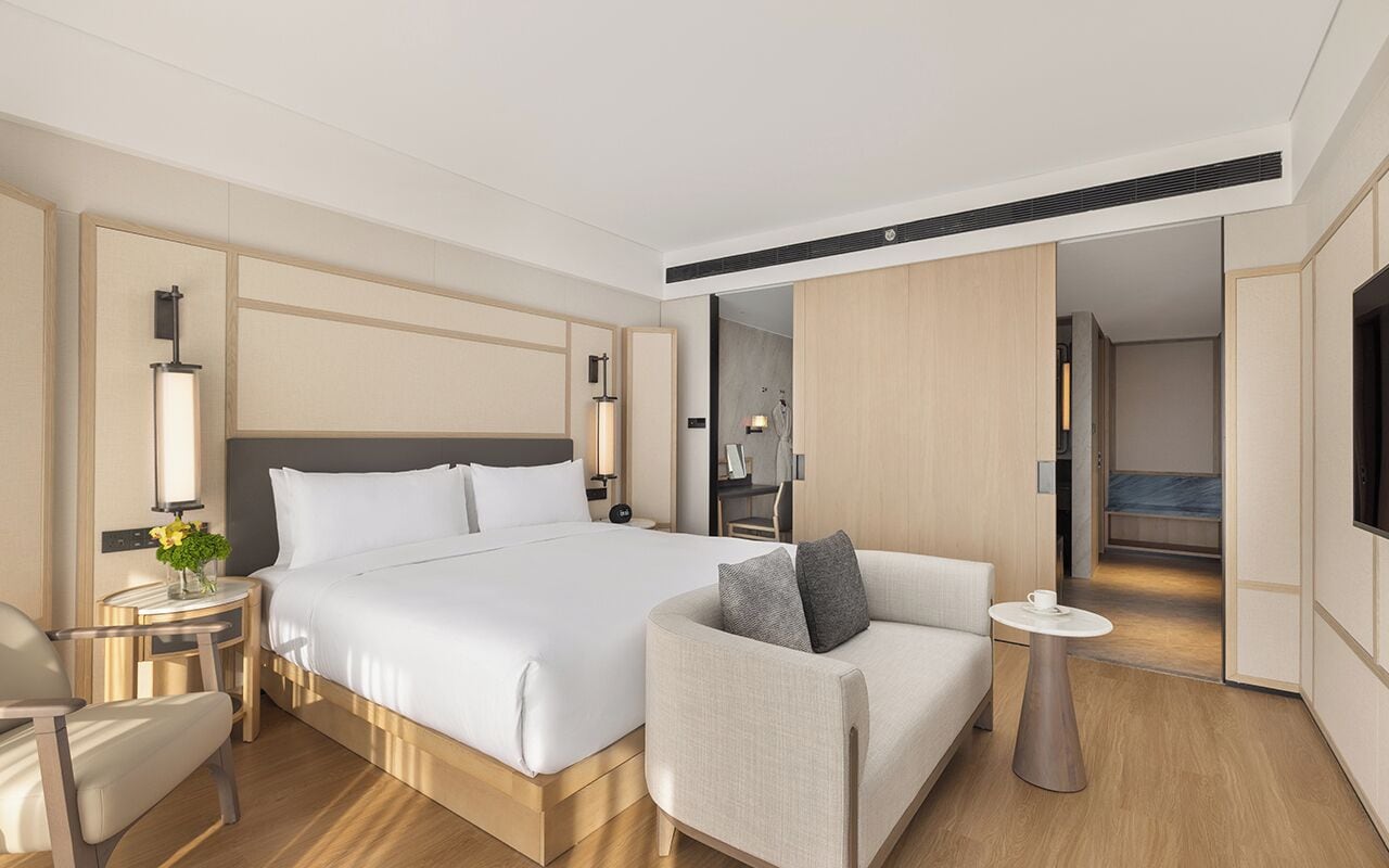 A modern hotel room with a large bed, a sofa, a small table, and a TV.