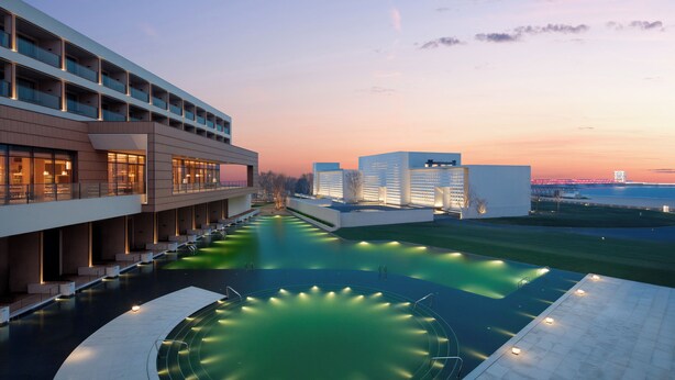 A modern hotel with a pool, multiple floors, and a waterfront view.