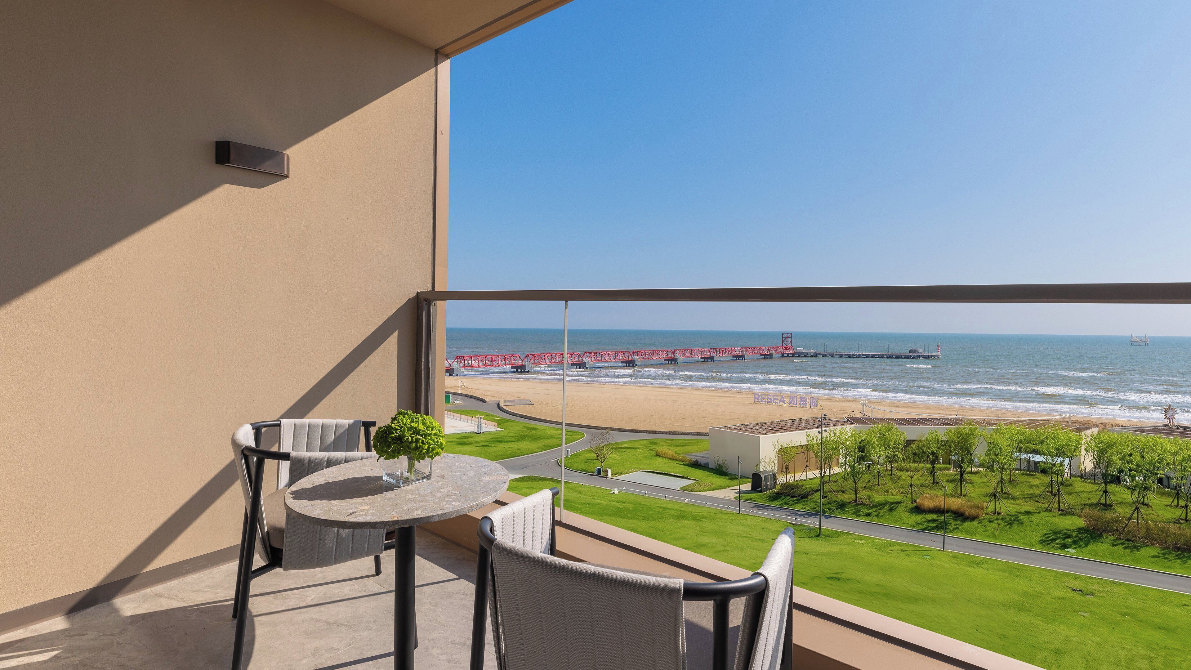 A balcony with a view of the beach, a red bridge, and a lighthouse.