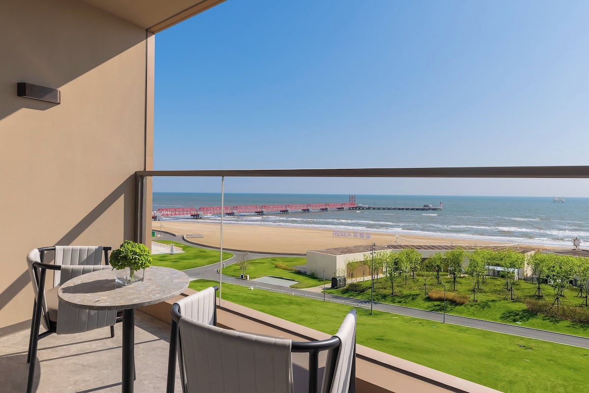 A balcony with a view of the beach, a red bridge, and a lighthouse.