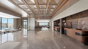 A spacious lobby with a high ceiling, a reception desk, and a large window offering a view of the city.