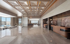 A spacious lobby with a high ceiling, a reception desk, and a large window offering a view of the city.