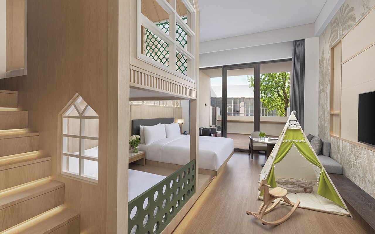 A hotel room with a loft bed, a tent-like play area, a dining area, and a large window.