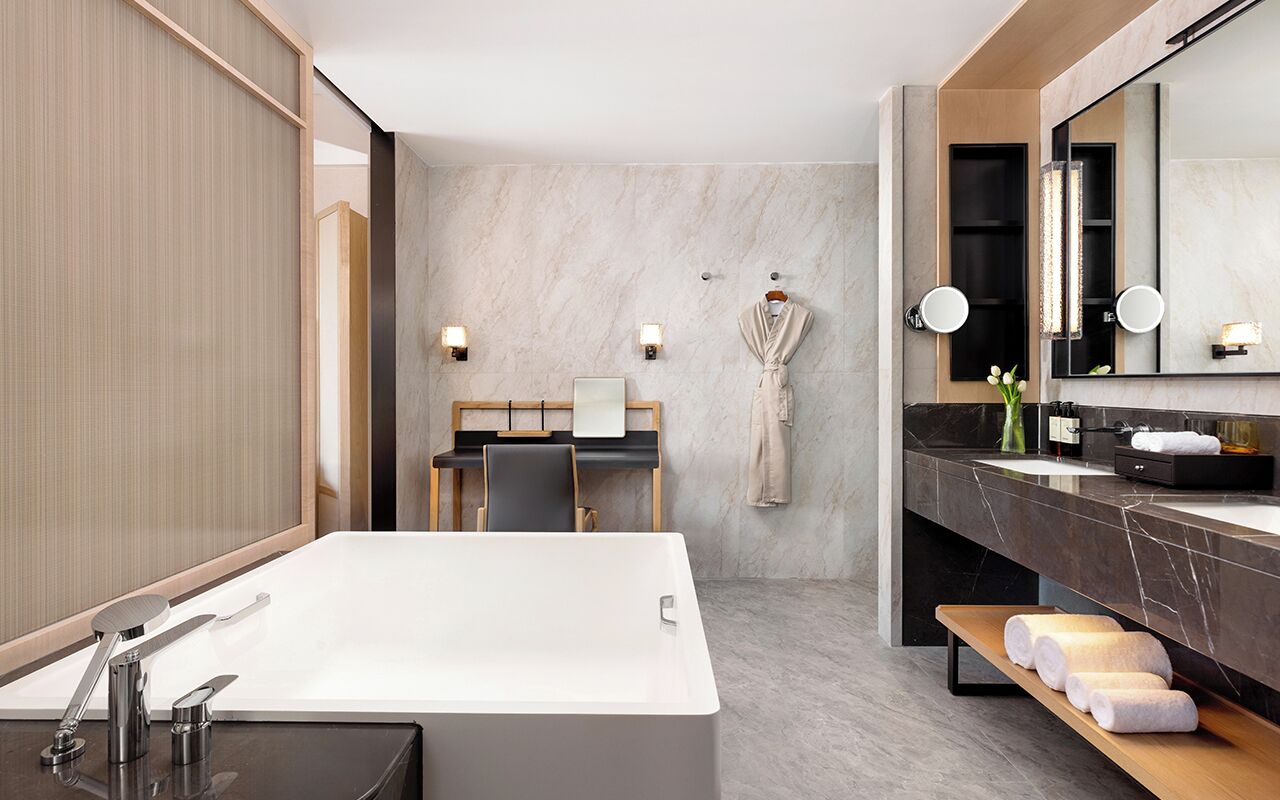 A modern bathroom with a large bathtub, a vanity with a mirror, and a seating area with a table and chairs.