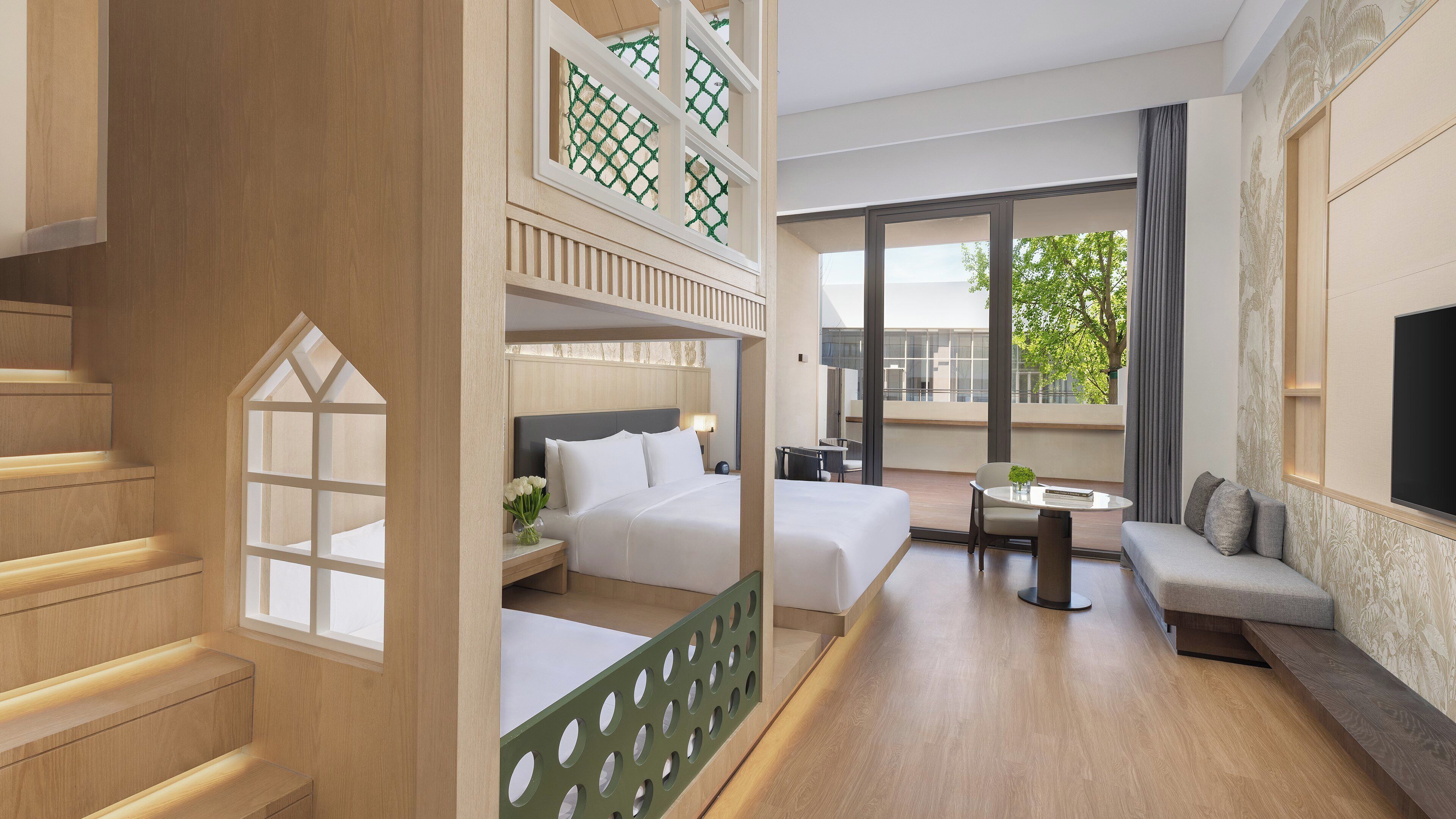 A hotel room with a balcony, a bed, a sofa, a small table, and a TV.