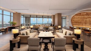 A spacious hotel lobby with a bar area, seating arrangements, and large windows offering a view.