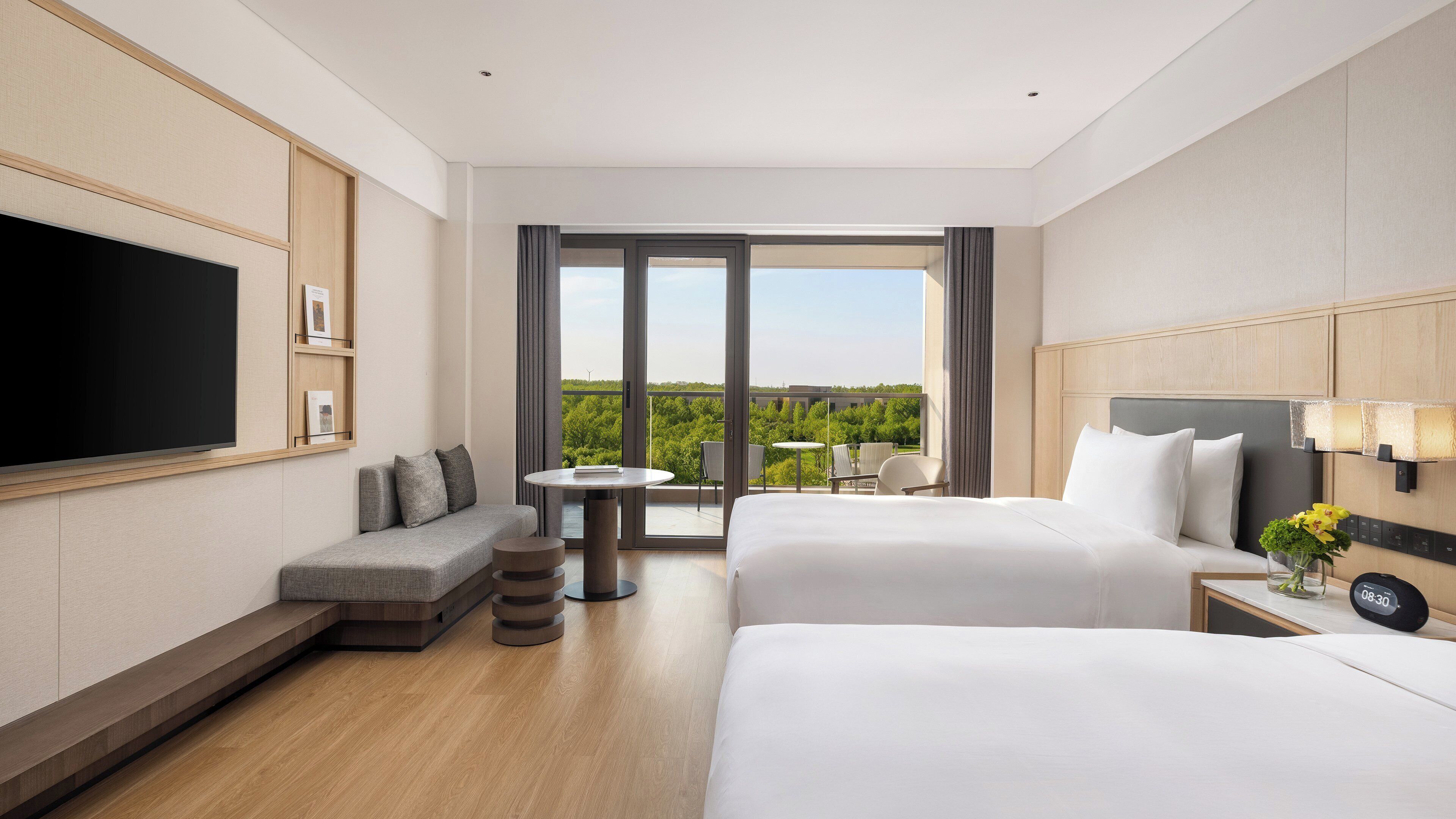 A hotel room with a TV, two beds, a sofa, a small table, and a balcony with a view.