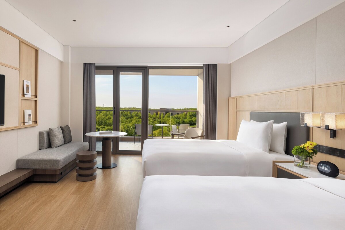 Une chambre d’hôtel équipée d’une télévision, de deux lits, d’un canapé, d’une petite table et d’un balcon avec vue.
