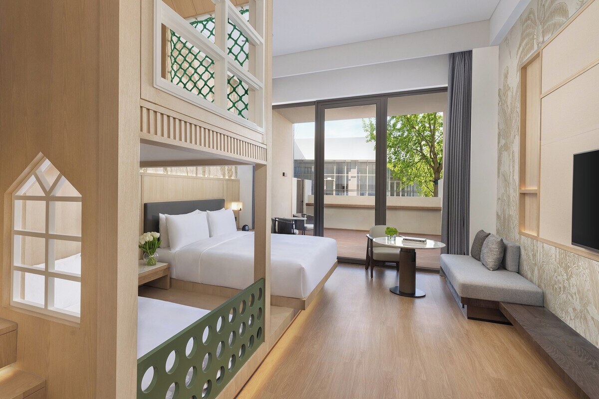 Une chambre d’hôtel avec un balcon, un lit, un canapé, une petite table et un téléviseur.