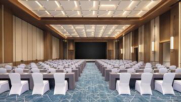 Un salón de conferencias con filas de mesas y sillas, una pantalla grande y una alfombra estampada.