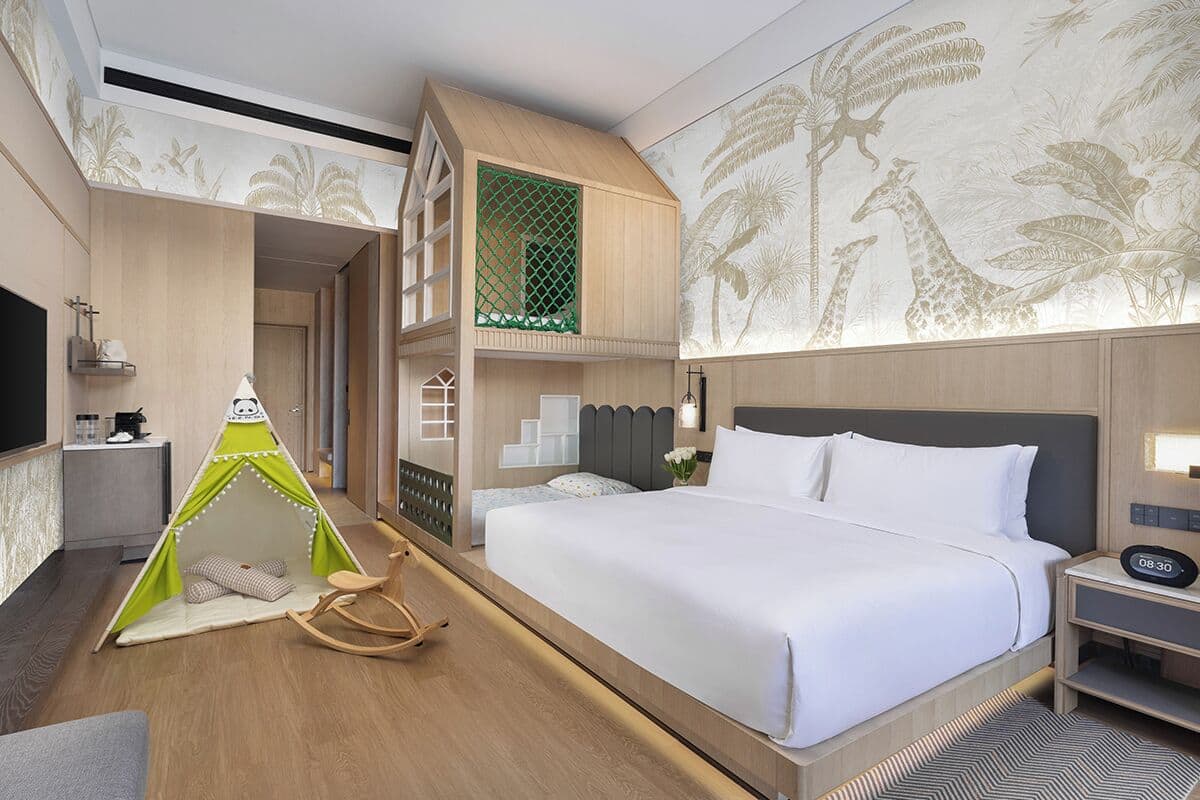 A hotel room with a large bed, a television, a green tent, and a wall with a giraffe mural.