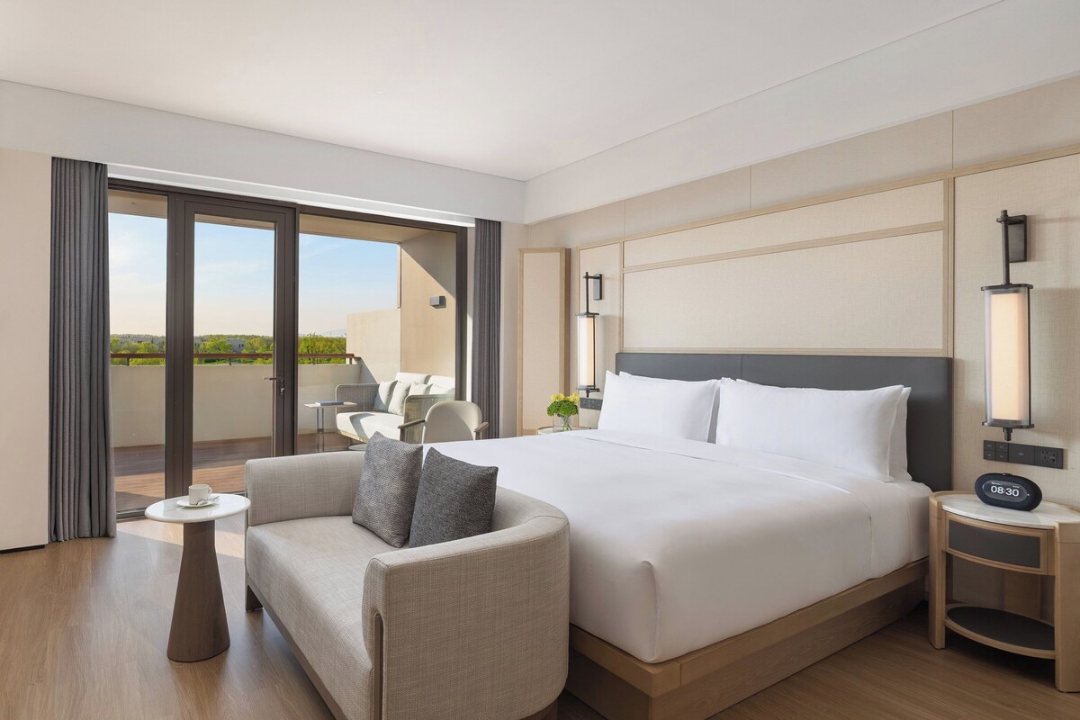 Une chambre d’hôtel avec un lit, une chaise, une petite table, une télévision et un balcon avec vue.
