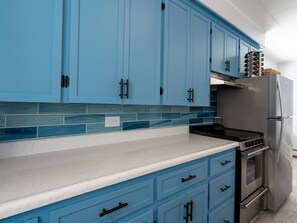 Une cuisine avec des armoires bleues, un réfrigérateur en acier inoxydable et une cuisinière noire.