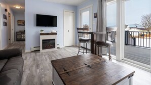 A living room with a fireplace, a television, a dining area with chairs, and a balcony with a railing.