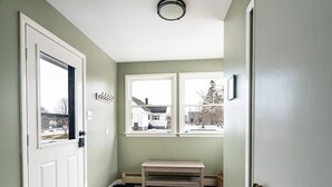A hallway with a bench, a door, and a window with a view of a house.