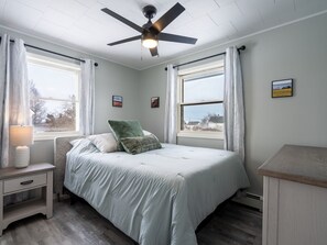 Une chambre à coucher avec un lit, une table de chevet, un ventilateur de plafond et une fenêtre avec des rideaux.