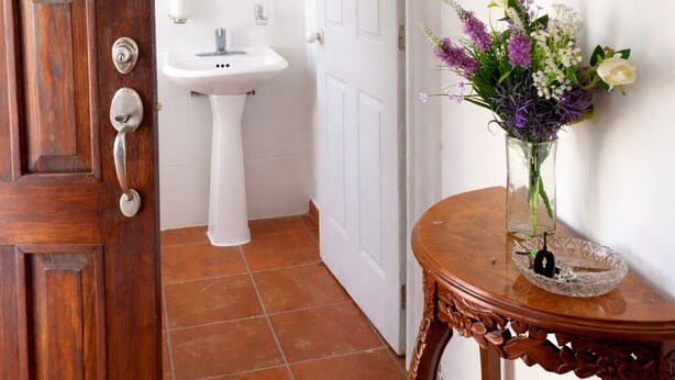 Eine Holztür, ein weißes Waschbecken, ein Spiegel und eine Vase mit Blumen.