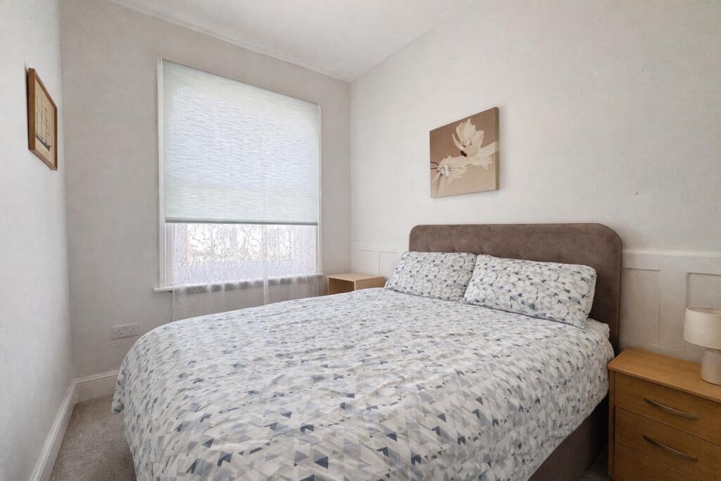 A bedroom with a bed, a nightstand, a window with blinds, and a wall-mounted artwork.
