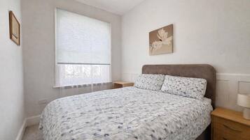 A bedroom with a bed, a nightstand, a window with blinds, and a wall-mounted artwork.