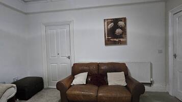 Une pièce avec un canapé en cuir marron, une porte blanche, un radiateur et un tableau encadré accroché au mur.