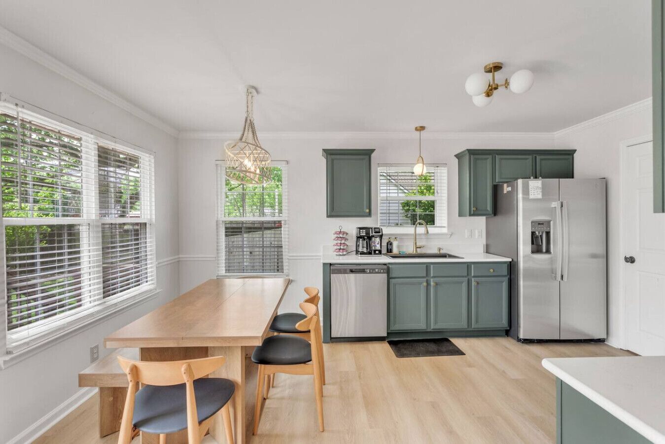 A modern kitchen with a dining area, featuring a wooden table, chairs, a refrigerator, and a coffee maker.