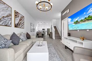 A modern living room with a sofa, coffee table, TV, and artwork. - The Majestic retreat by Disney (Davenport)