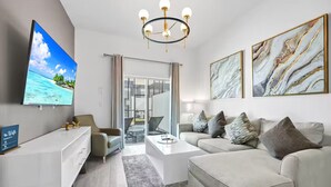 Ein modernes Wohnzimmer mit Flachbildfernseher, einer Chandelüster, einer Couch und einem Couchtisch.