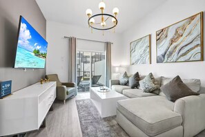 A modern living room with a flat-screen TV, a chandelier, a sofa, and a coffee table. - The Majestic retreat by Disney (Davenport)