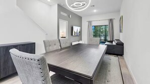 A modern dining room with a large table, grey upholstered chairs, a dark wood table, and a unique circular ceiling light. - The Epic Retreat by Disney (Davenport)