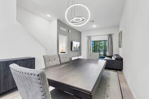 Uma sala de jantar moderna com uma mesa grande, cadeiras estofadas cinzas, mesa de madeira escura e uma luminária de teto circular singular.