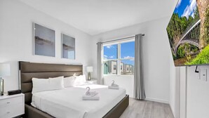 Una habitación de hotel moderna con una cama grande, televisión y ventana con cortinas.