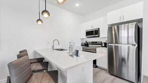 Una cocina moderna con armarios blancos, electrodomésticos de acero inoxidable y una isla central con asientos.