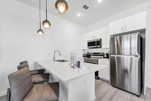A modern kitchen with white cabinetry, stainless steel appliances, and a central island with seating. - The Enchanted ReTreat by Disney (Davenport)