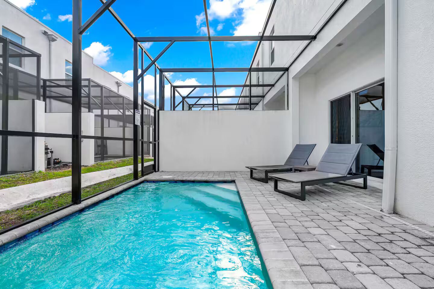 En pool med en glasvägg runt om, två solstolar och en klarblå himmel.